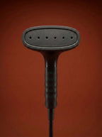 J-4000 Jiffy garment steamer with a black head, silver metal rod, light gray control base, and black cord, displayed on a round red pedestal against a warm rust-orange studio background - Sold by: Best Steamers