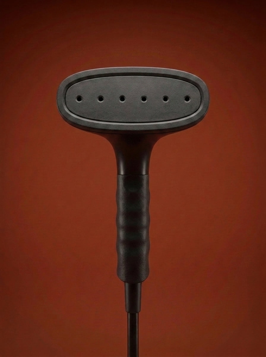J-4000 Jiffy garment steamer with a black head, silver metal rod, light gray control base, and black cord, displayed on a round red pedestal against a warm rust-orange studio background - Sold by: Best Steamers